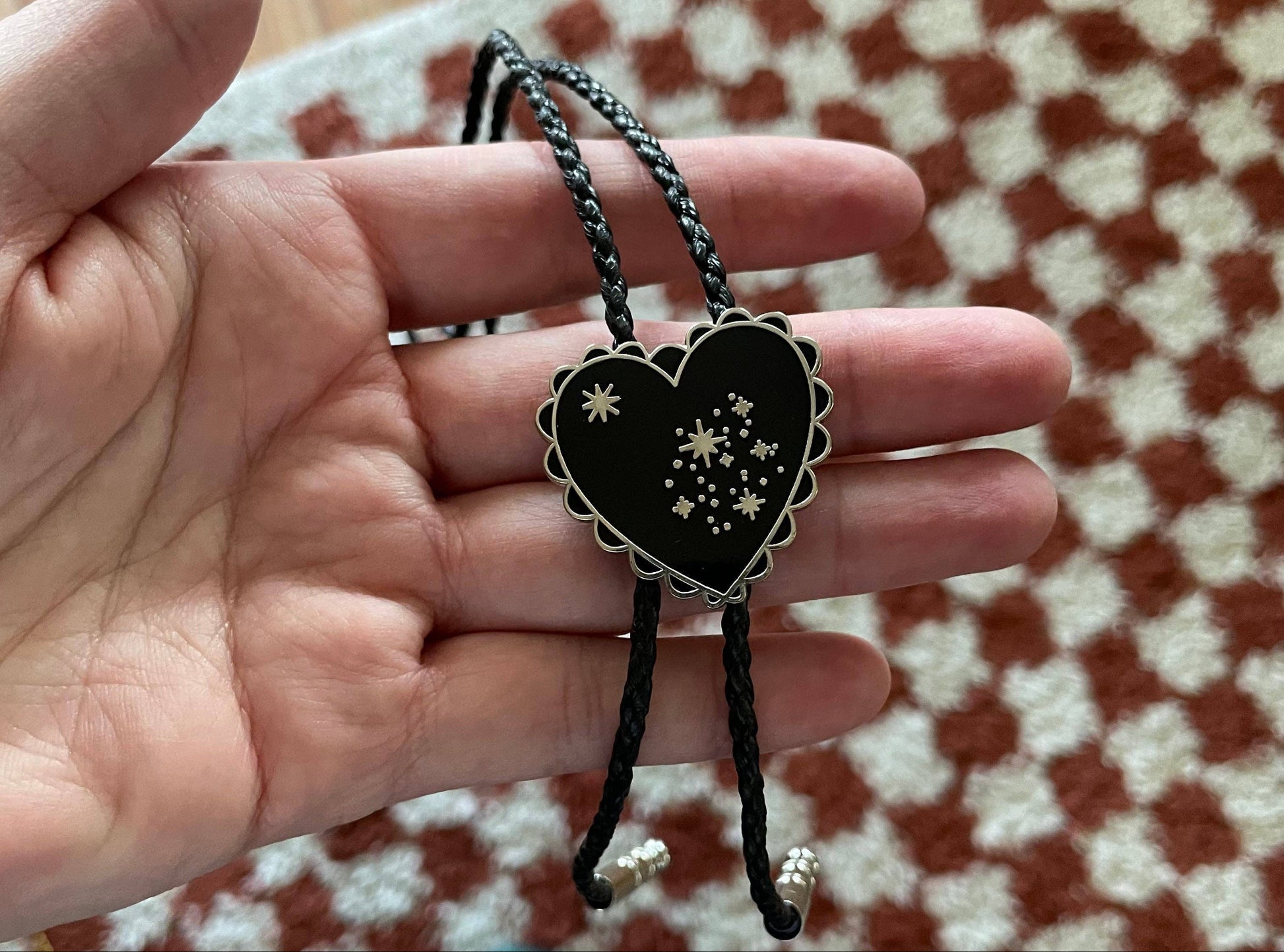 Heart-shaped pendant with star design held by a hand on a checkered floor.